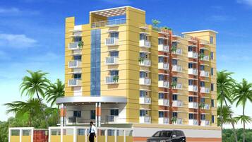 Un edificio residencial de varios pisos con balcones, un acceso cubierto y un automóvil estacionado frente a él.