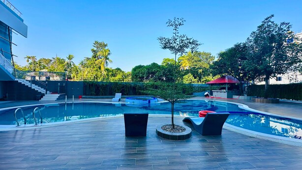 A swimming pool with a modern design, surrounded by a paved deck and a few trees. - Hotel Khan Palace (Kalapara)
