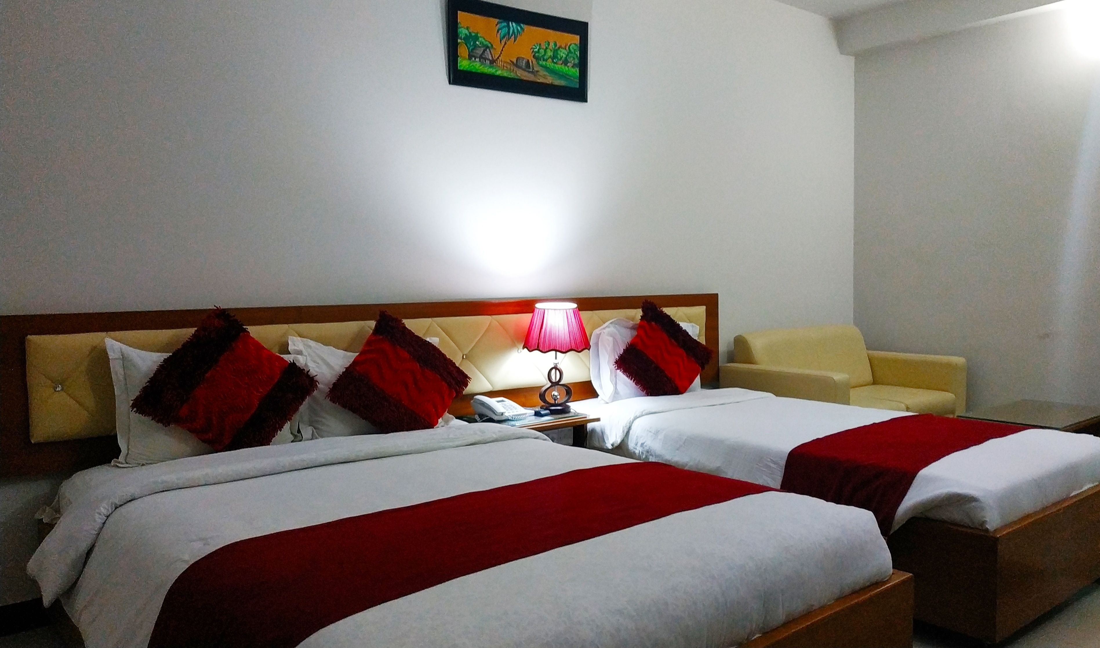 Una habitación de hotel con dos camas, una mesita de noche, una lámpara y un cuadro en la pared.