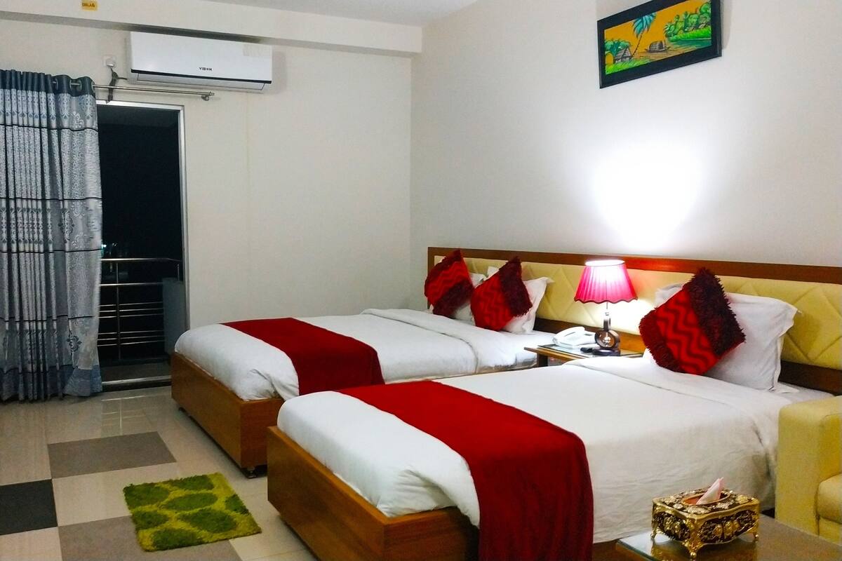 A hotel room with two beds, a TV, a bedside lamp, and a small table with a tissue box.