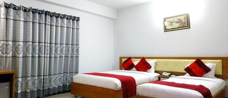 A hotel room with two beds, a wooden headboard, a bedside table, and a curtain with a floral pattern.