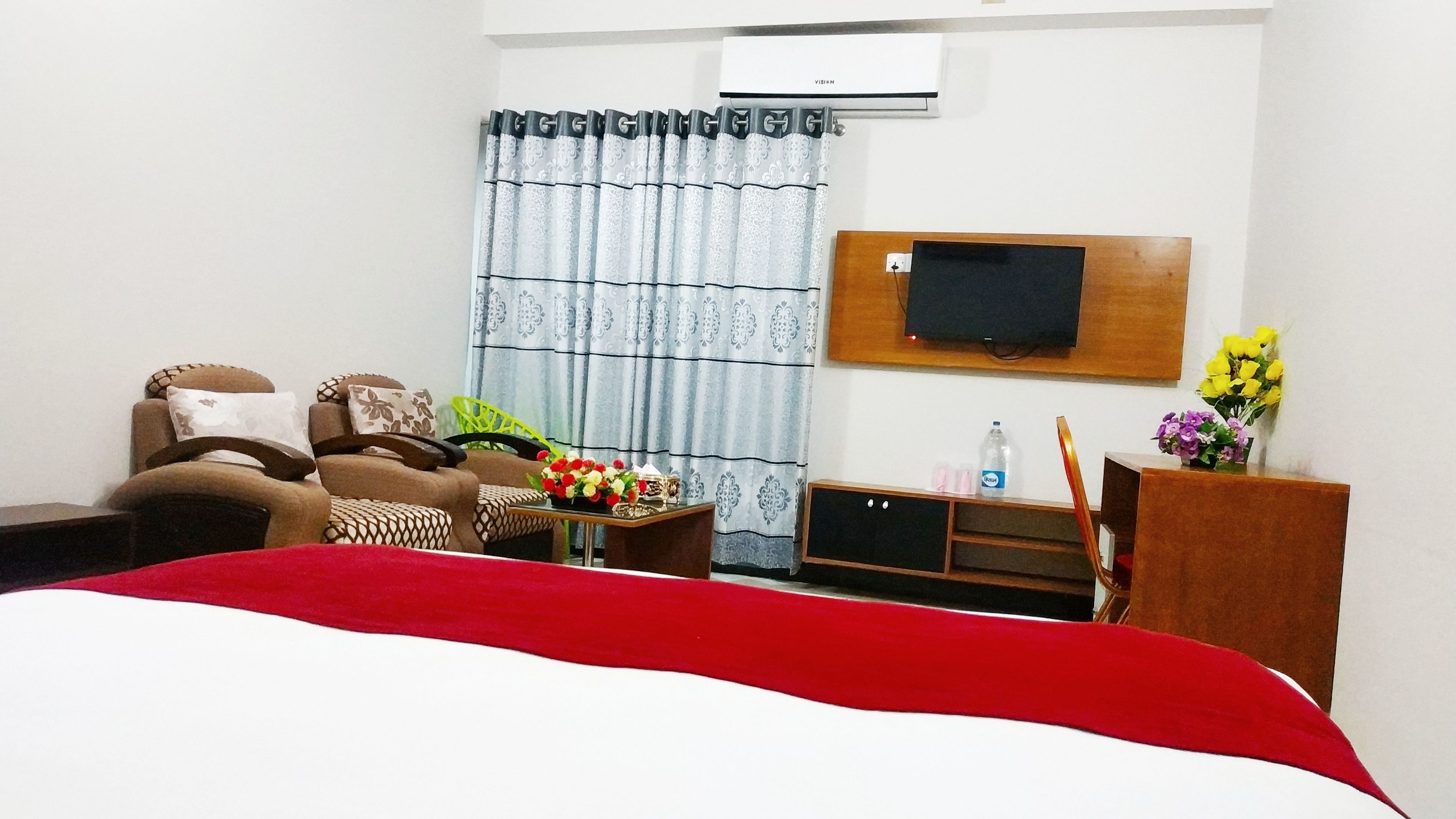 A hotel room with a bed, a sofa, a TV, a desk, and a window with curtains.