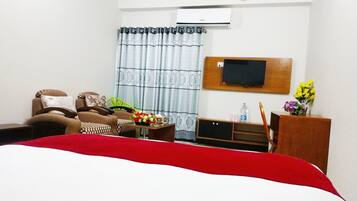 A hotel room with a bed, a sofa, a TV, a desk, and a window with curtains.