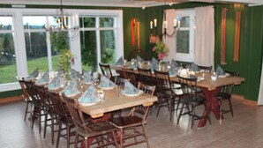A dining area with multiple tables and chairs, large windows, and a view of the outdoors. - Mesnabakken pensjonat (Ringsaker)