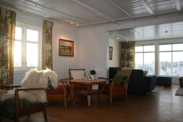 Una habitación con una mesa de comedor de madera rodeada de sillas, un sofá y una ventana con vistas a árboles.