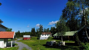 Cenário rural com um caminho de cascalho que leva a um celeiro vermelho, uma casa branca e um edifício com telhado verde.
