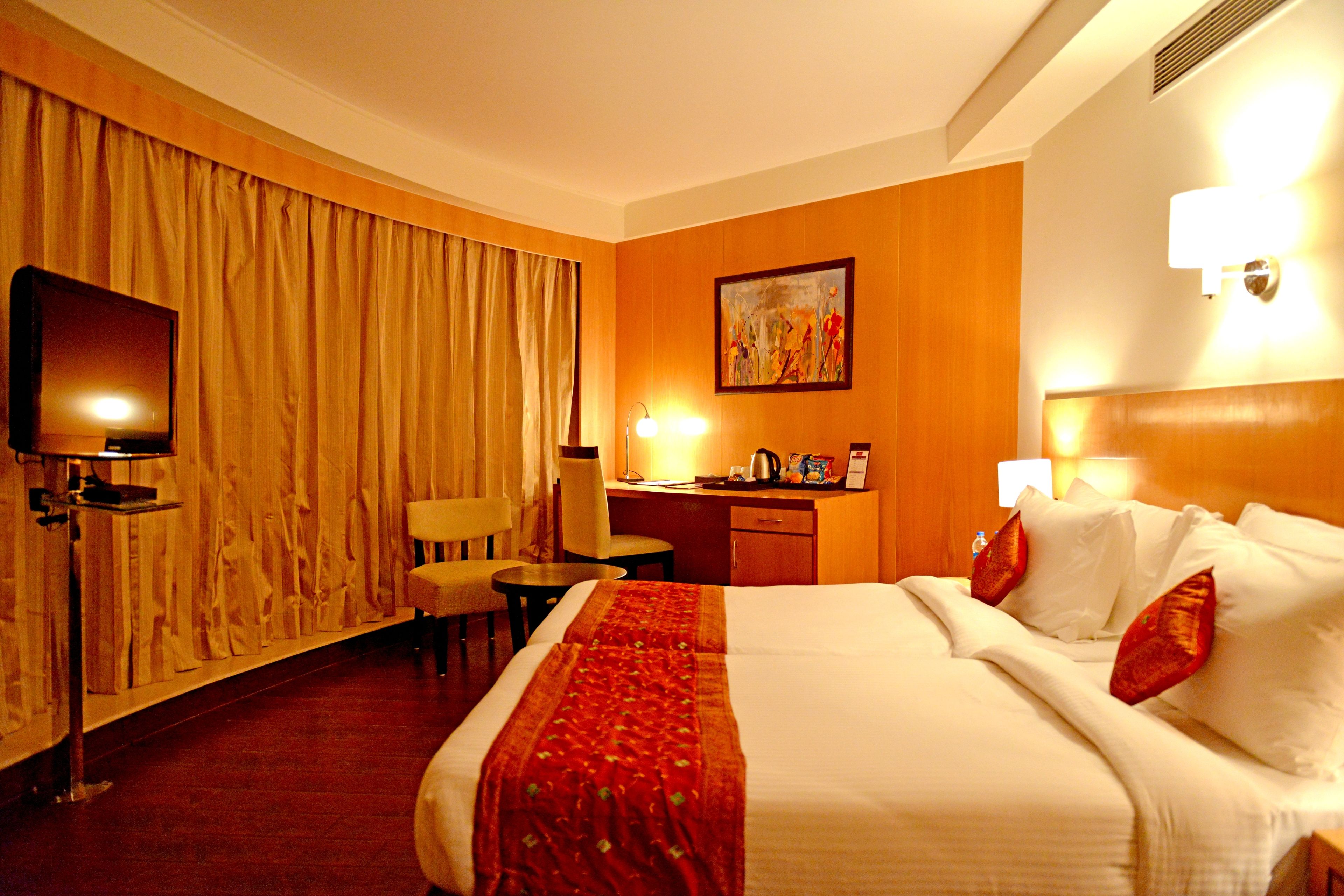 A hotel room with a large bed, a desk, a chair, a television, and a painting on the wall.