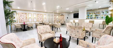 A spacious lounge area with patterned chairs, a central table, and a bar with a variety of bottles.