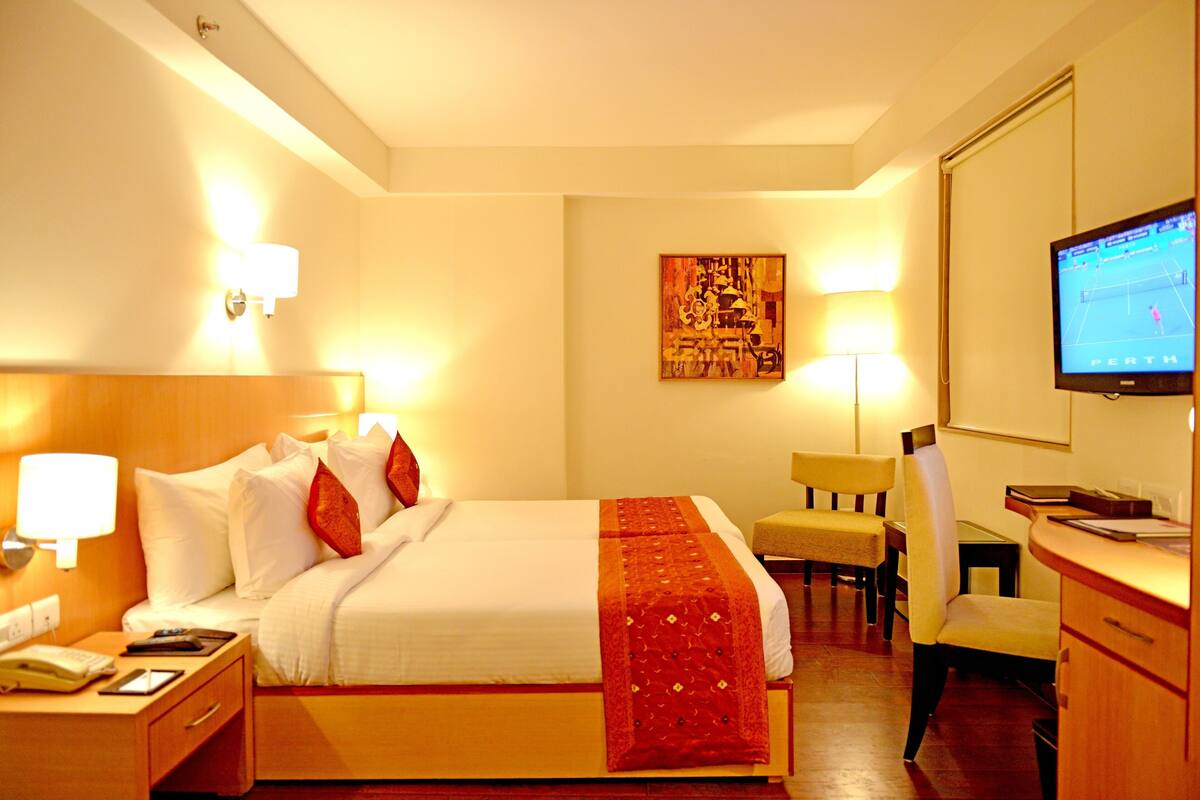 Une chambre d’hôtel comprenant un lit, des tables de chevet, un bureau avec une chaise, une télévision et des œuvres d’art accrochées au mur.