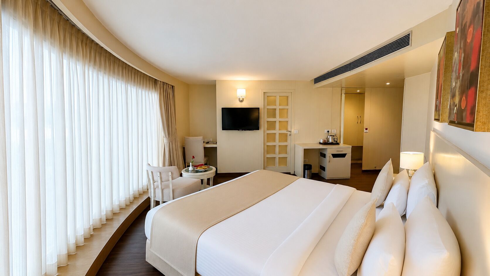 Habitación de hotel con una cama grande, un escritorio, una silla, un televisor y un baño visible a través de una puerta abierta.