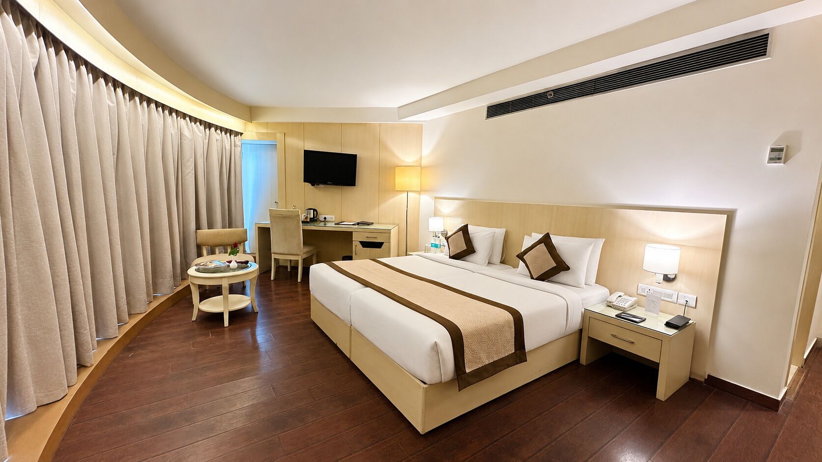 Une chambre d’hôtel comprenant un lit, une table de chevet, un bureau, une chaise et des rideaux.