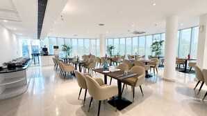A spacious dining area with multiple tables and chairs, large windows, and a buffet counter. - The Theme Hotel Jaipur (Jaipur)