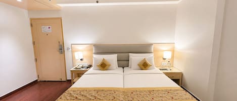 Une chambre d’hôtel avec un lit double, deux tables de chevet avec des lampes, une porte en bois et une couvre-lit à motifs.