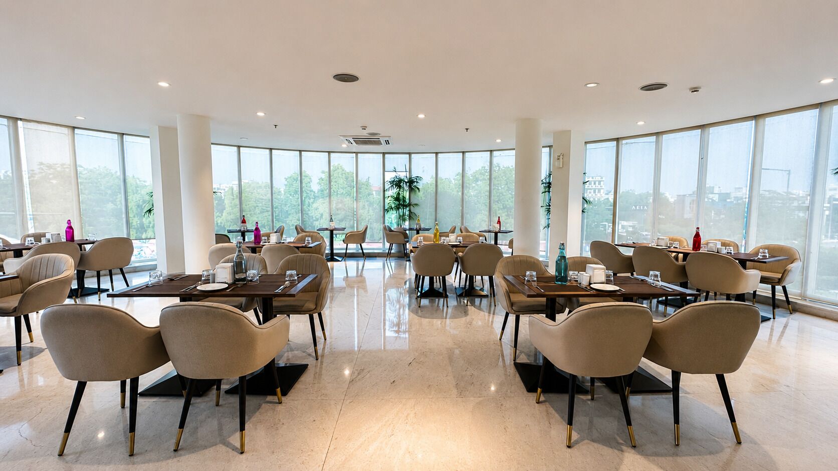 A spacious, modern dining area with multiple tables and chairs, large windows offering views of the city, and a clean, polished floor.