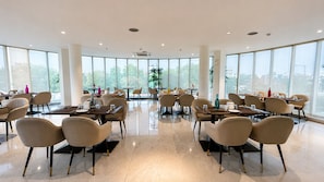 Un espace de restauration spacieux et moderne, doté de nombreuses tables et chaises, de grandes fenêtres offrant une vue sur la ville, et d’un sol propre et bien entretenu.