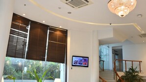A spacious living area with a sofa, coffee table, and TV, a staircase, and a large window with blinds. - The Theme Hotel Jaipur (Jaipur)