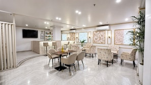 A modern dining area with a round table and chairs, a bar with a TV, and framed artwork on the walls. - The Theme Hotel Jaipur (Jaipur)