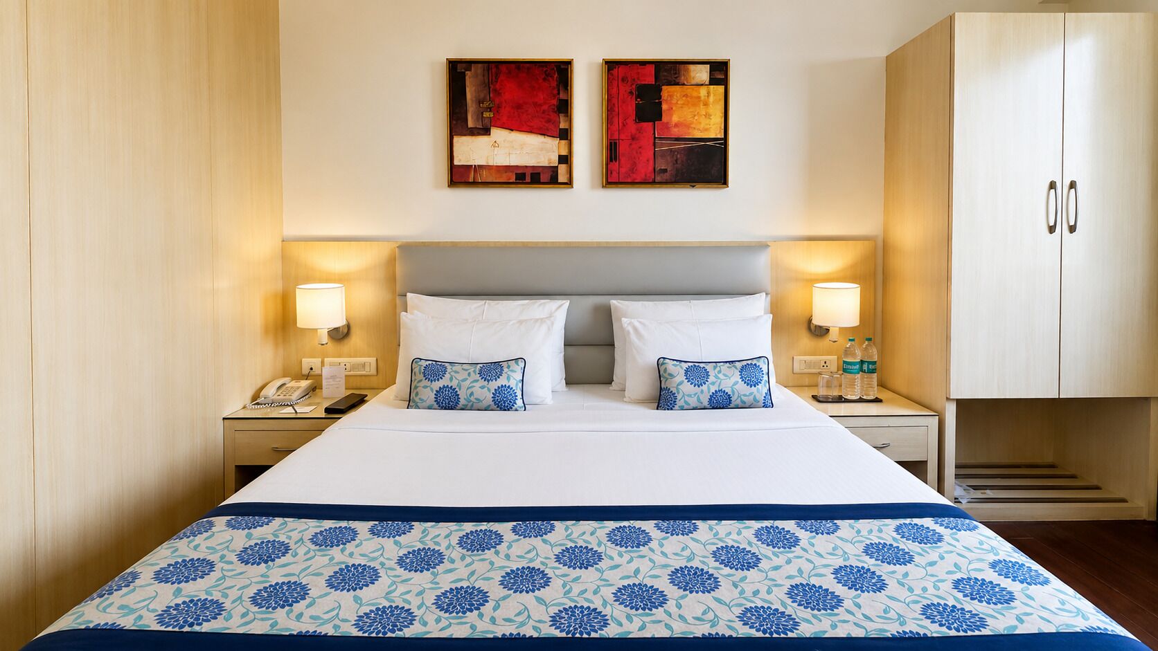 A hotel room with a bed, two bedside lamps, a telephone, a water bottle, and a cabinet.