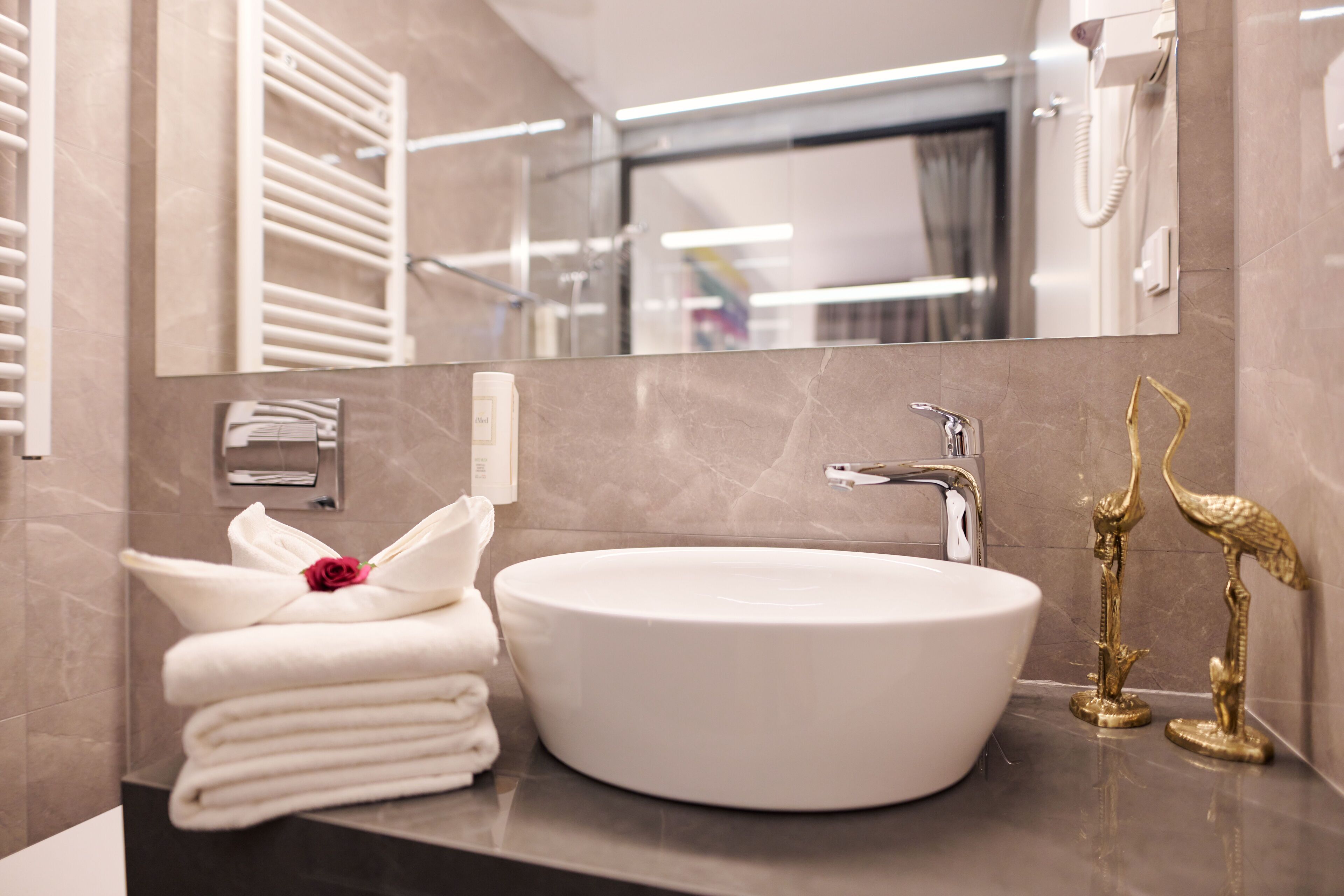 A modern bathroom with a round white sink, a towel rack with folded towels, a mirror, and two golden bird-shaped sculptures.