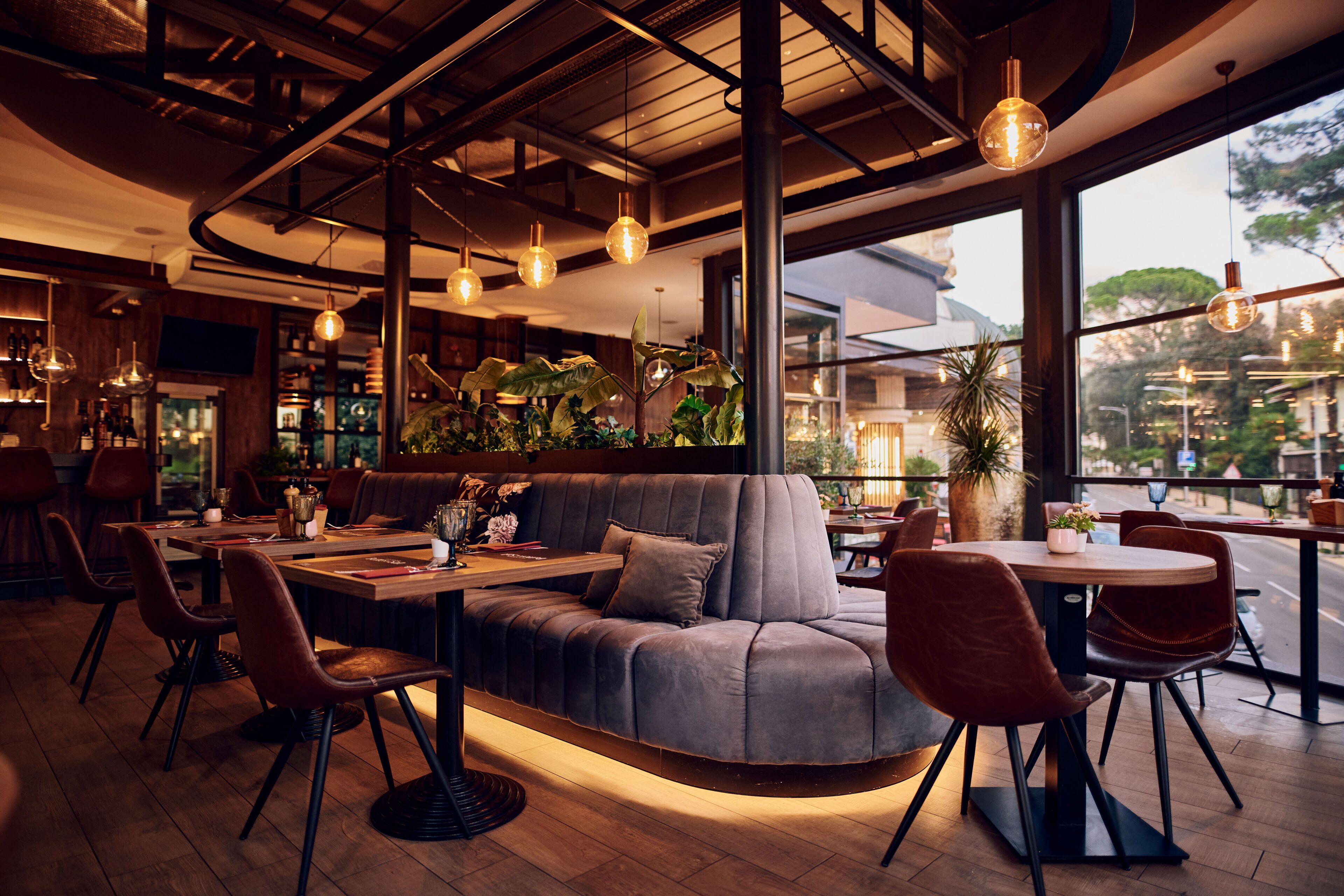 Un interior de restaurante moderno con un sofá curvo, mesas redondas y lámparas colgantes.