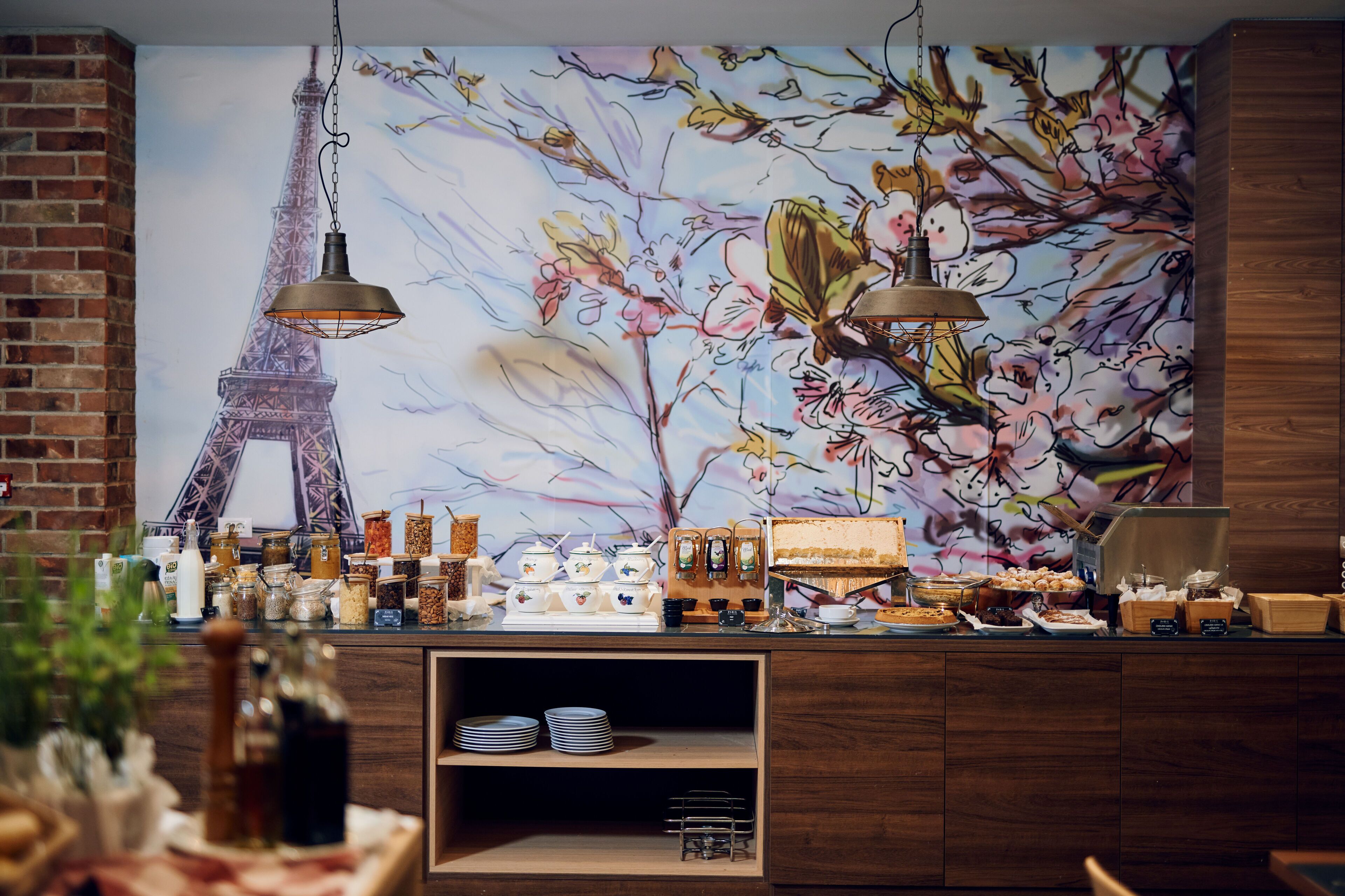 Un caffè con un murale della Torre Eiffel e decorazioni floreali, scaffali in legno con stoviglie e lampade pendenti.