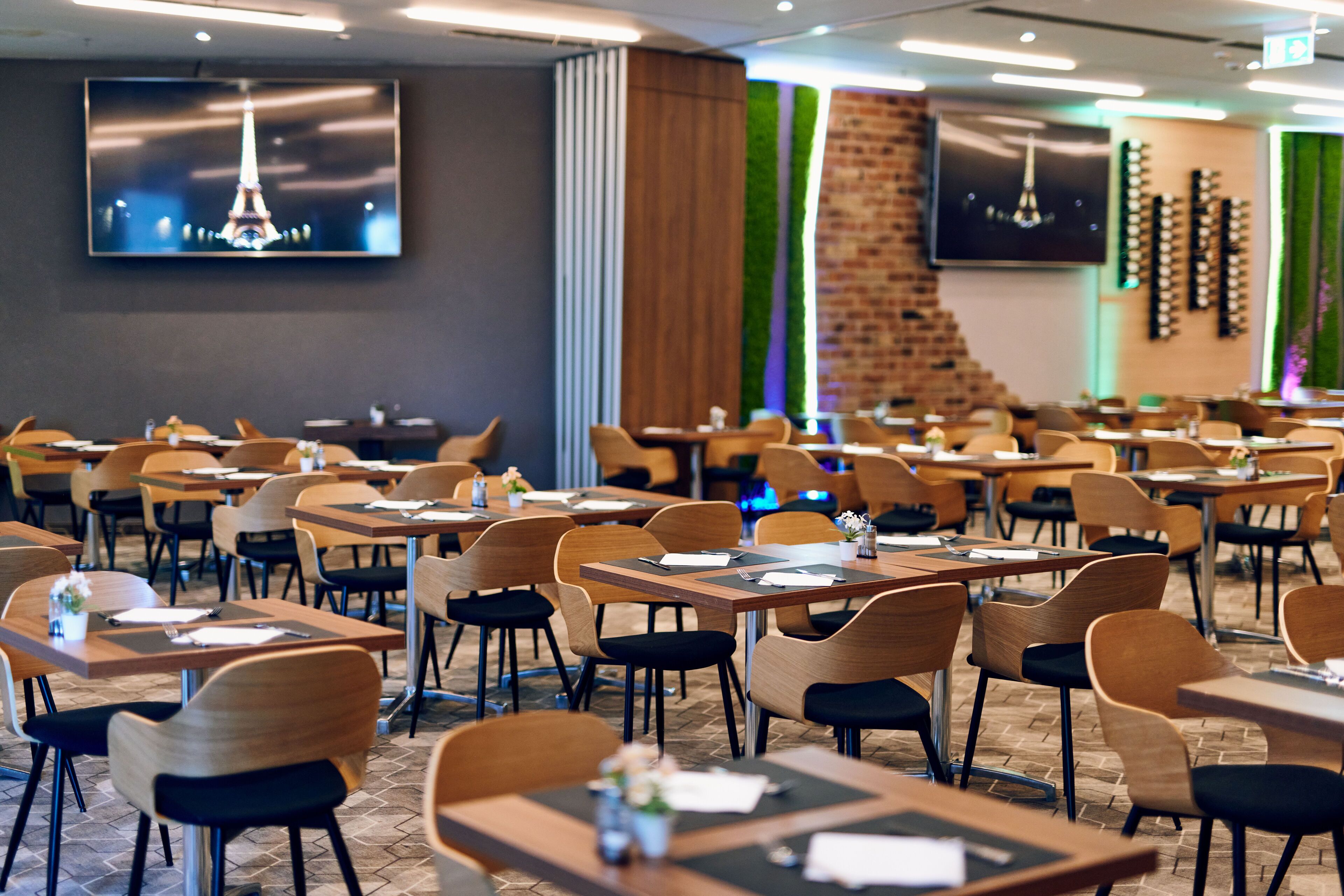 A restaurant with multiple tables and chairs, a brick wall, and two flat-screen TVs mounted on the wall.