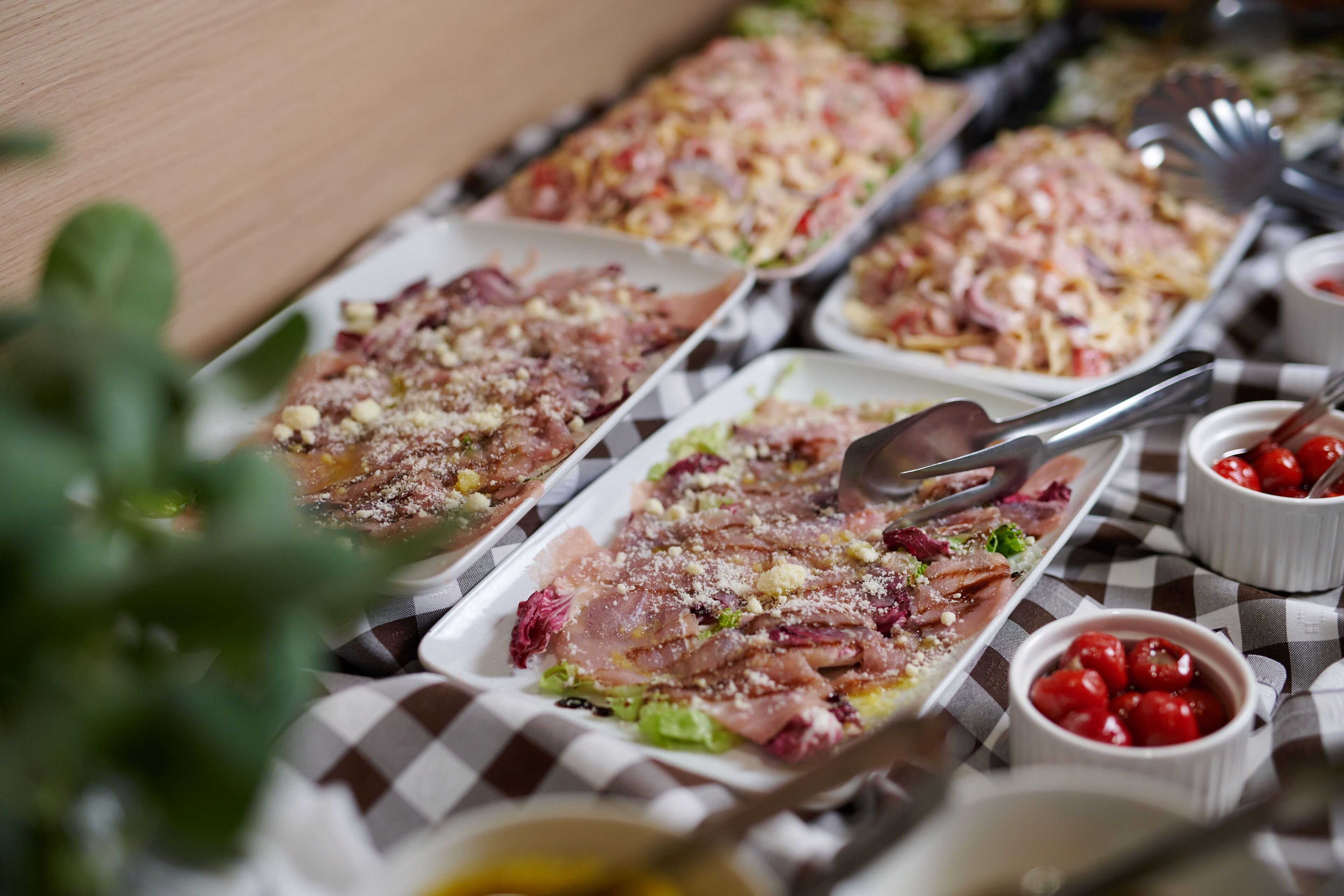 Una mesa de bufé con diversos platos, incluyendo pasta, ensaladas y una variedad de carnes, sobre un mantel a cuadros.