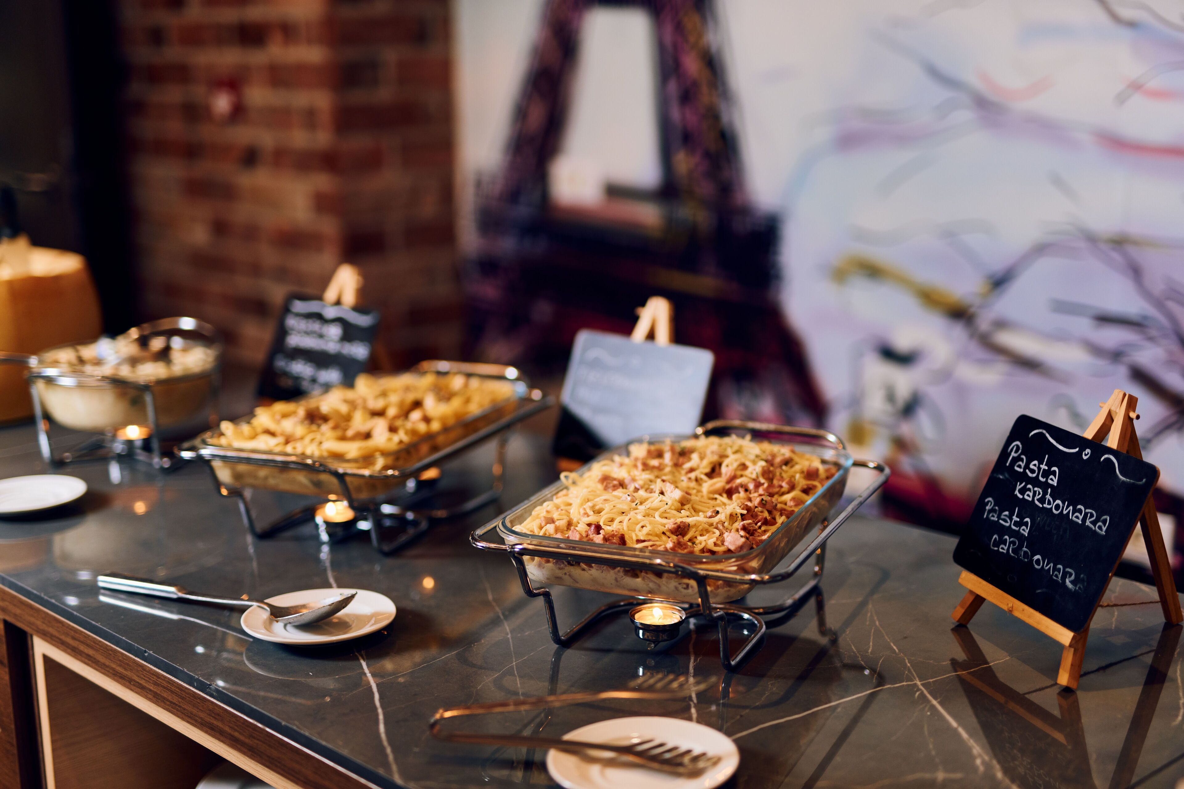 Ein Buffett mit verschiedenen Speisen, darunter Pasta Carbonara, und ein Kreidetafel mit den Namen der Gerichte.
