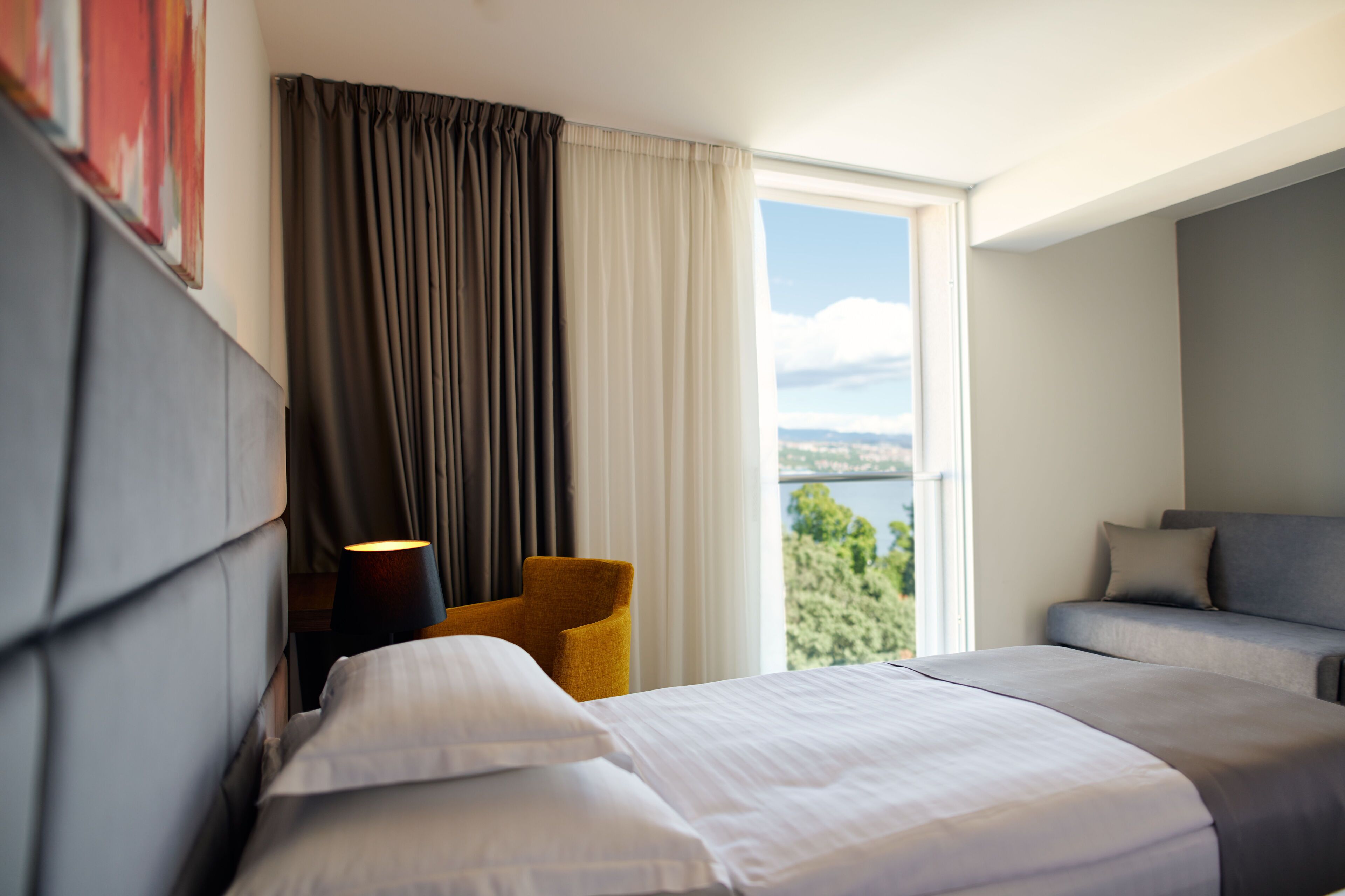 A hotel room with a bed, a sofa, a chair, and a view of a body of water.