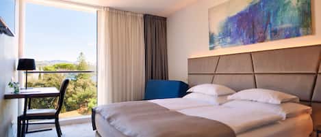 A hotel room with a large bed, a desk with a chair, a painting on the wall, and a view of the outdoors.