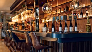 Una zona de bar con una barra larga, varios taburetes y una gran variedad de botellas y vasos.
