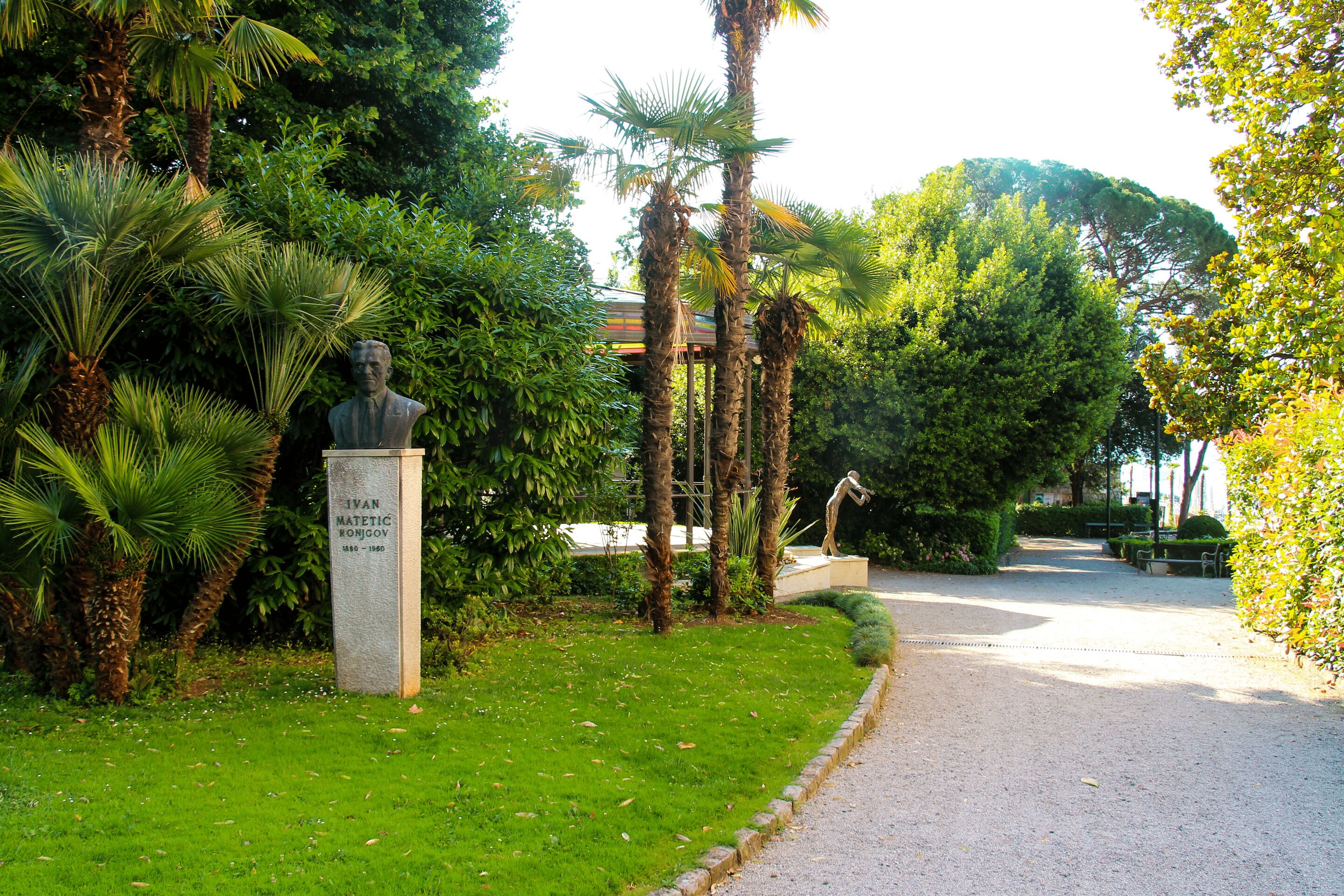 A statue in a park with a pathway and benches.