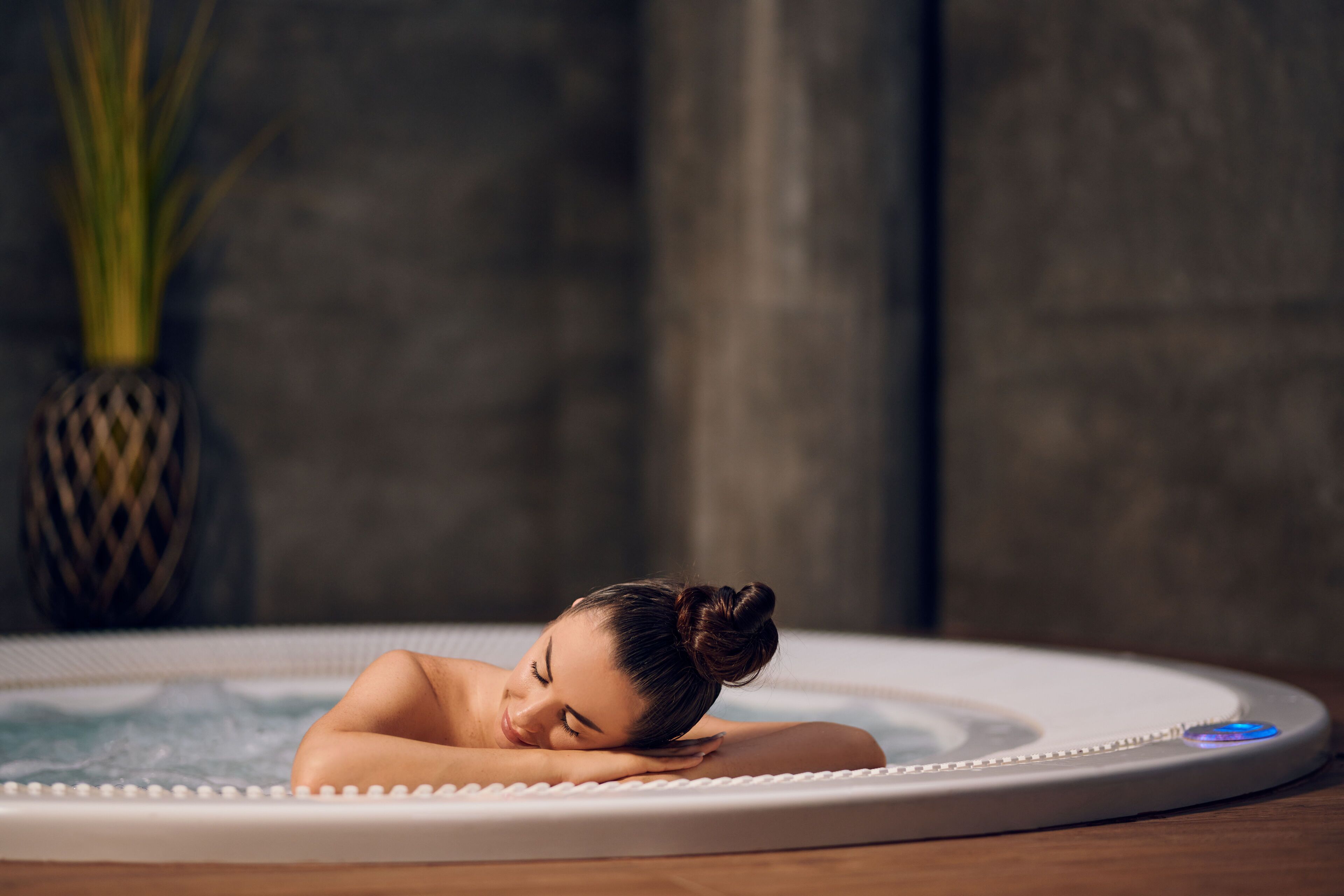 Una persona relajándose en un jacuzzi con piso de madera y un jarrón decorativo al fondo.