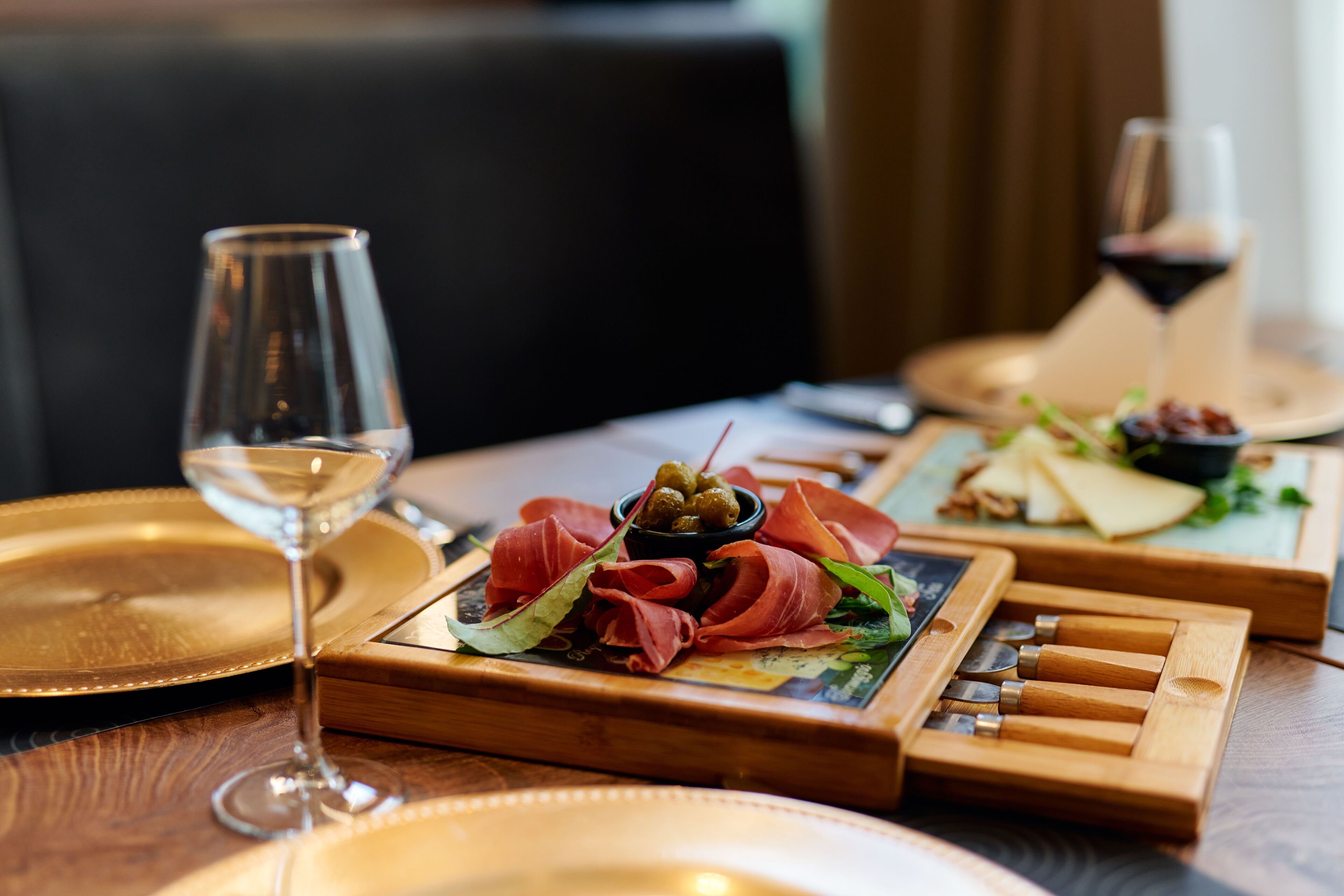 A wooden board with various food items and a wine glass on a table.