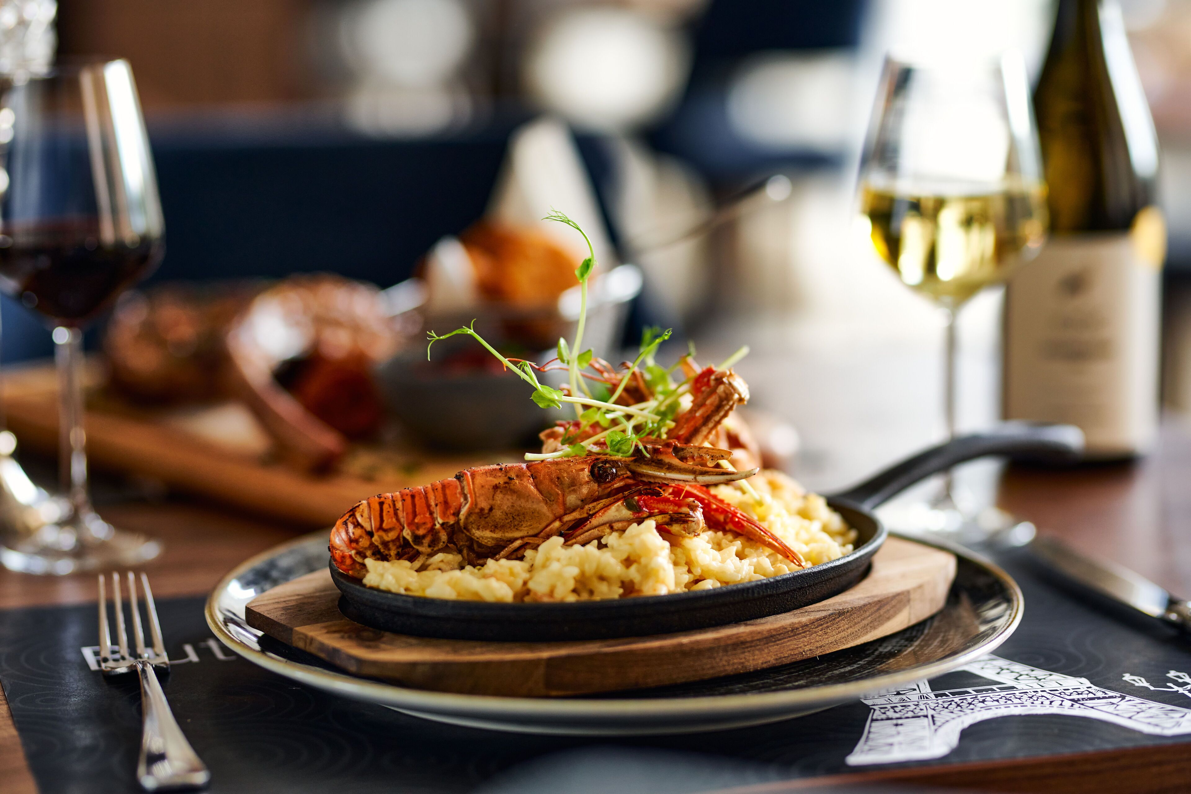 Un plato de langosta con un tenedor y cuchillo a un lado, una copa de vino y una botella sobre la mesa.