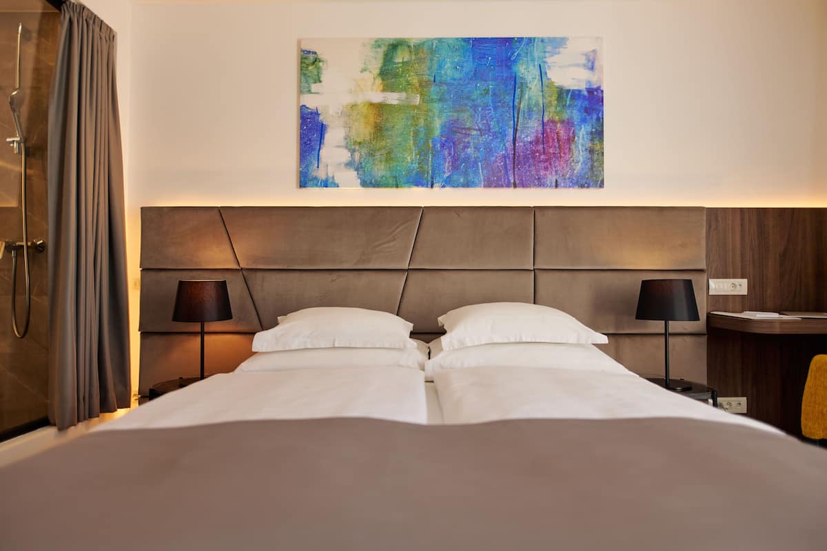 A hotel room with a large bed, two bedside tables with lamps, a headboard with a geometric design, and a colorful abstract painting on the wall.