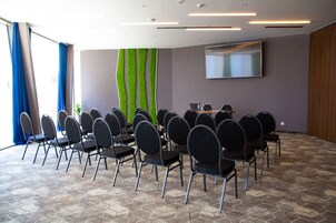 A conference room with a large table surrounded by chairs, a flat-screen TV on the wall, and a patterned floor.