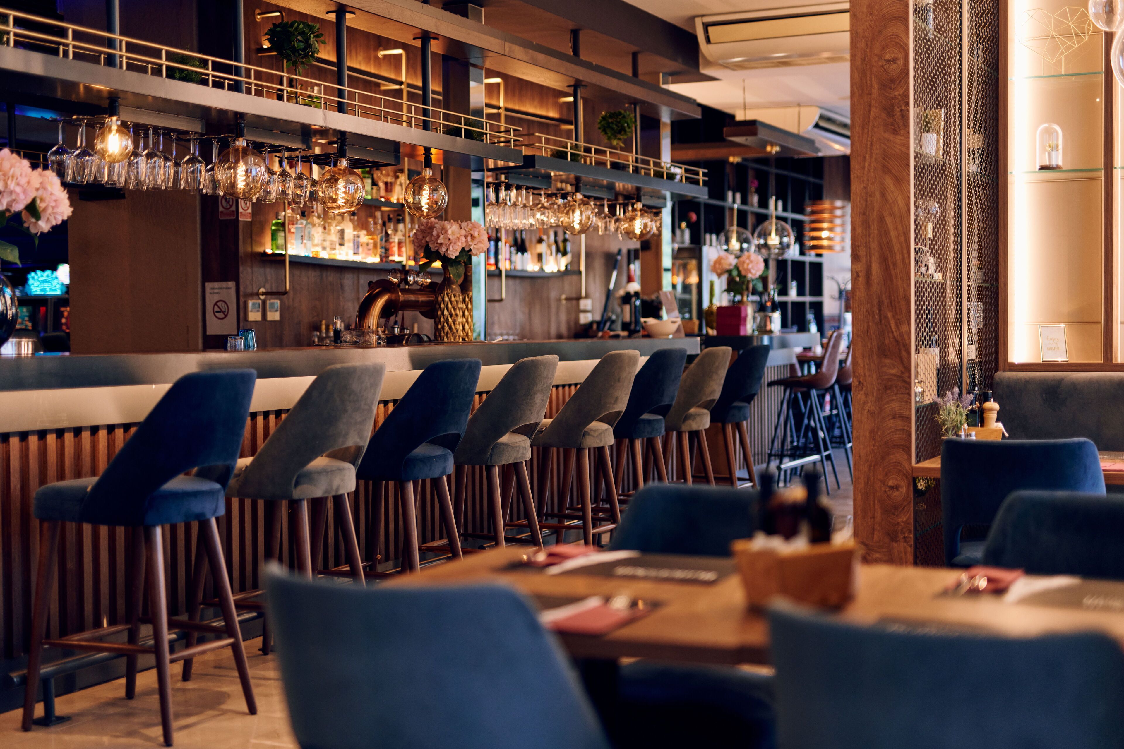 A bar area with multiple seating options, including bar stools and tables, and a variety of bottles and glasses on shelves.