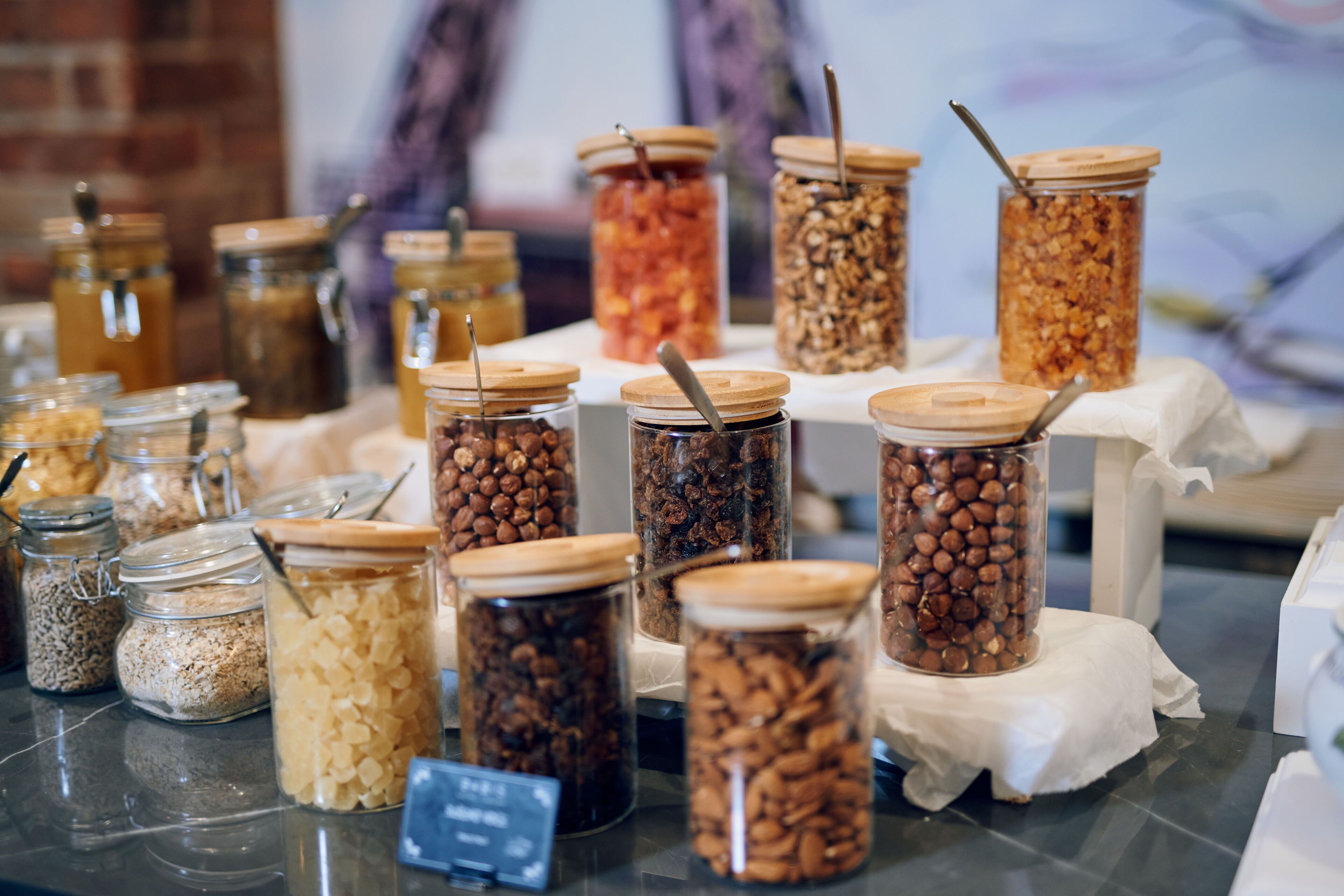A variety of food items in glass jars with wooden lids, displayed on a table with a white cloth.