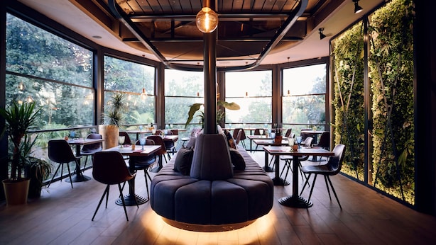 Un restaurante moderno con una zona de estar central, ventanas amplias y una pared verde.