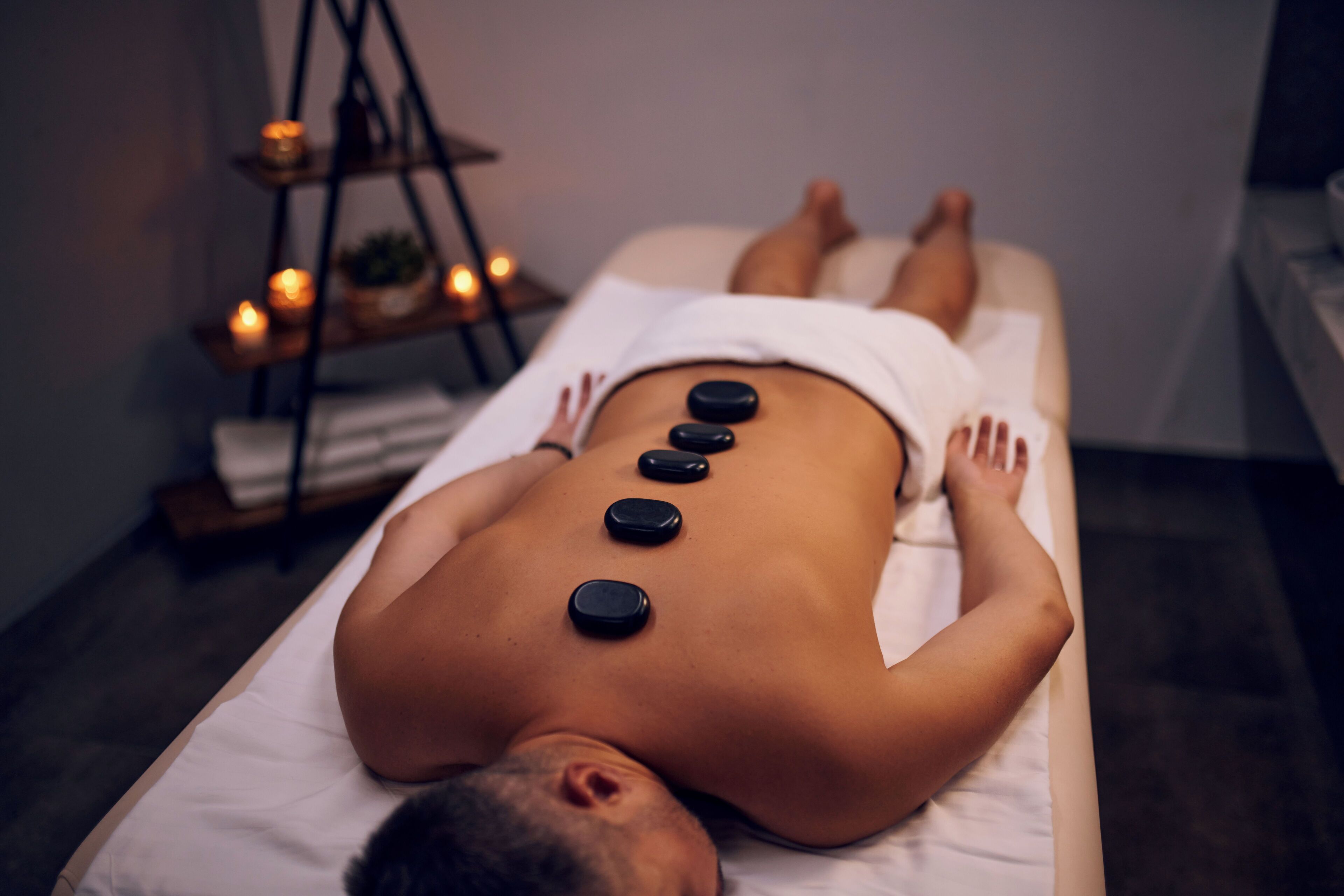 Una persona recibiendo un tratamiento de masajes en la espalda con piedras calientes.