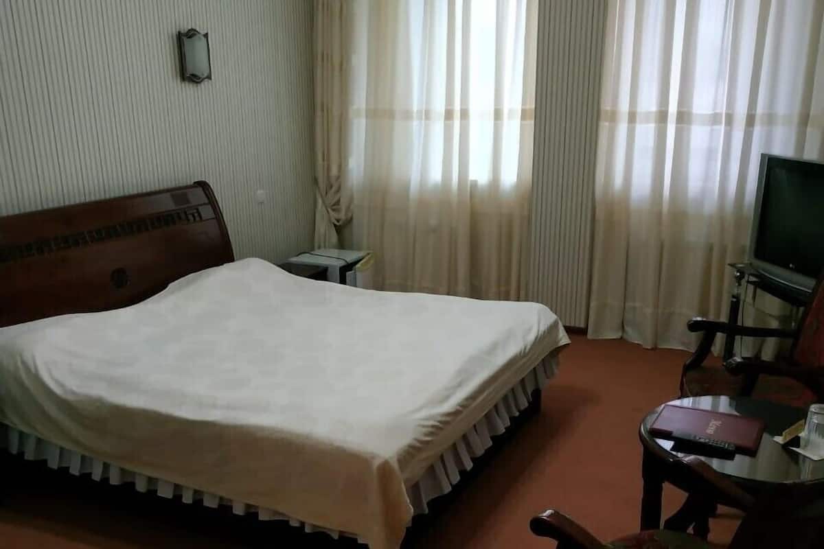 A hotel room with a large bed, a television, a small table with a chair, and a window with curtains.