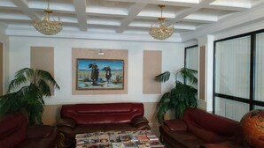 Una habitación con un sofá de cuero rojo, una mesa con revistas, un cuadro enmarcado y dos plantas en macetas.