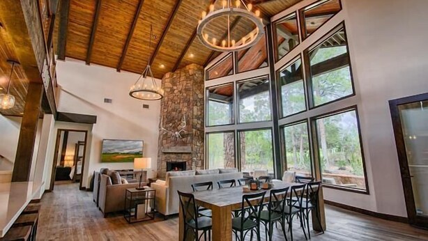 A spacious living area with a fireplace, large windows, and a dining table.