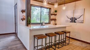 A kitchen with a large island, bar stools, pendant lights, a window with a view, and a bull painting on the wall.