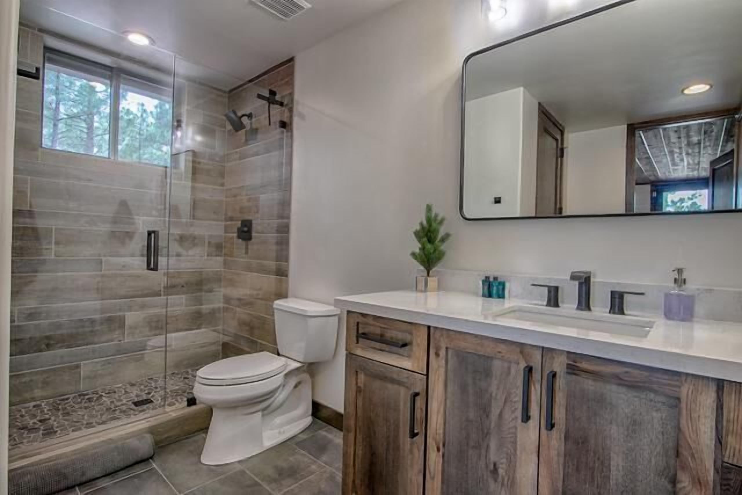 A modern bathroom with a glass shower enclosure, a white toilet, and wooden cabinets.