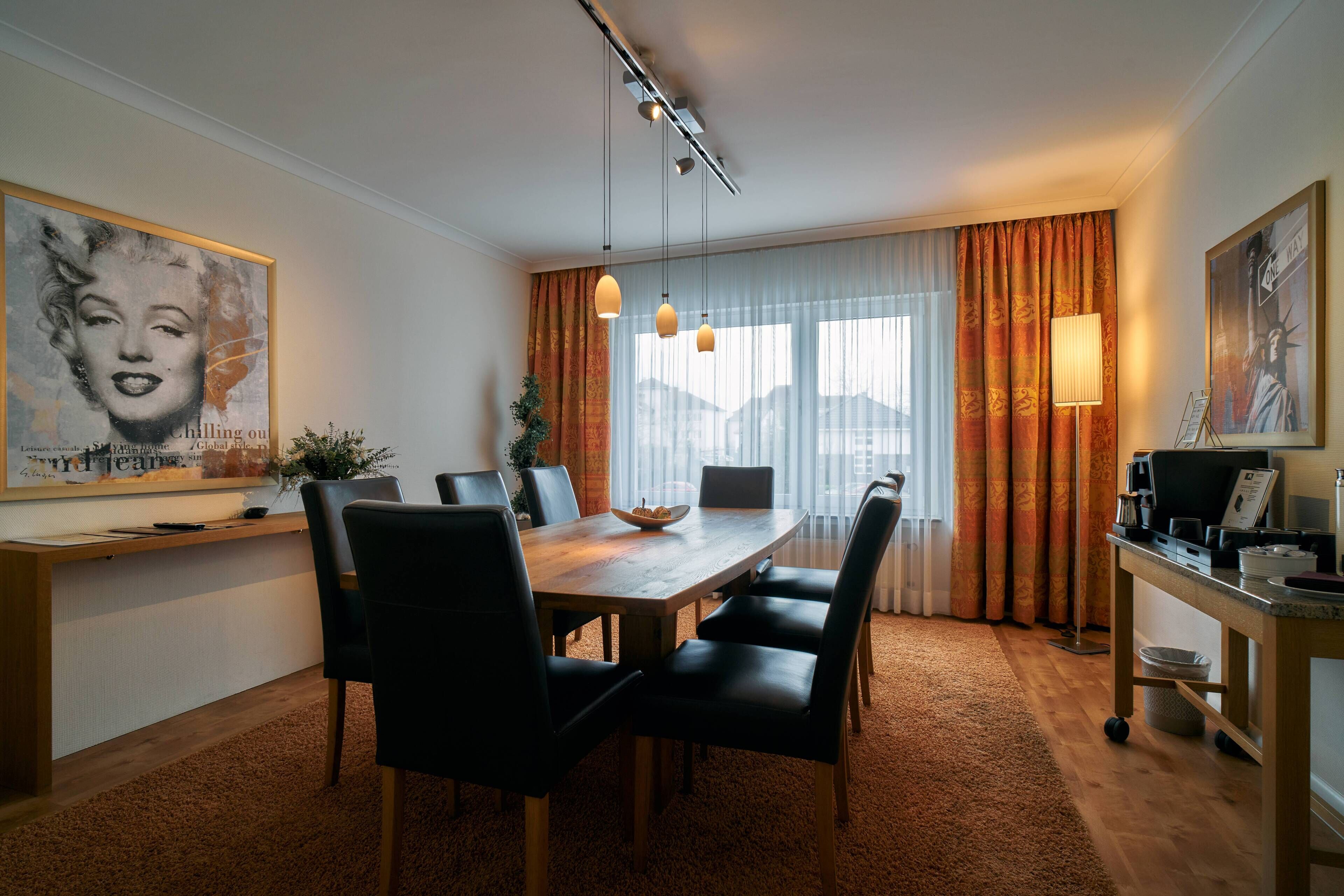 A modern dining area with a wooden table and black chairs, a large framed artwork on the wall, and a view of the city through large windows with orange curtains.
