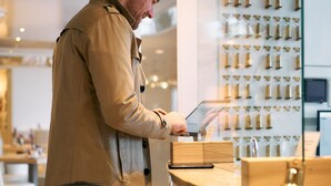 A person using a tablet at a counter in a modern, well-lit room with a display of items on the wall behind. - Hotel Engbert (Oelde)
