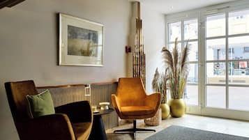 A modern lobby with a wooden bench, a single armchair, a framed artwork on the wall, and a large window with a view of the street.