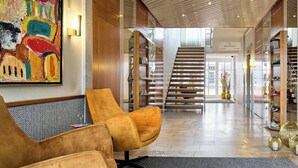 A modern lobby with a reception desk, a staircase, and a large abstract painting. - Hotel Engbert (Oelde)
